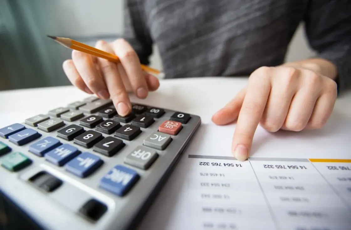 Imagen que muestra las manos de una persona con un lápiz tecleando la calculadora mientras observa si le cuadran los cálculos