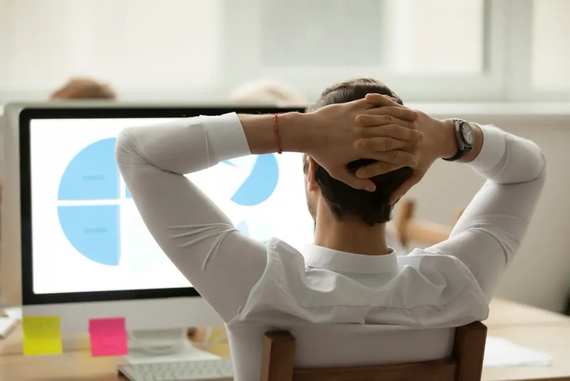 Imagen que muestra a un hombre de espaldas sentado con los brazos sujetando su cabeza mientras mira una gráfica en el monitor de su ordenador